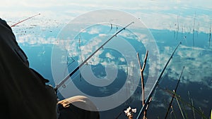 Fishing rod in the hands of a fisherman. Lake shore. Smooth calm and calm water with reflection of clouds. Beautiful