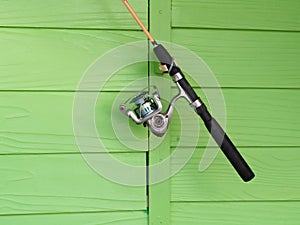 Fishing rod is hung on a green wooden wall.