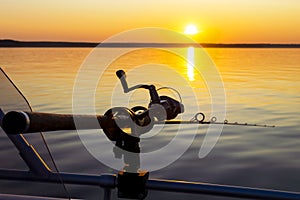 Fishing rod spinning with the line close-up. Fishing rod in rod holder in fishing boat due the fishery day at the sunset. Fishing