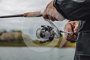 Fishing rod with a spinning reel in the hands of a fisherman on an overcast spring day.