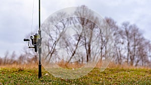 Fishing rod spinning reel stands on the background of the field.