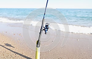 The fishing rod stands on the sand on the seashore, blurry