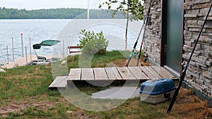 Fishing rods lean against a cabin wall, near a dock on the lake in the distance.