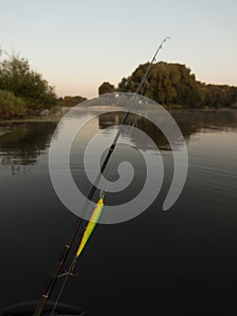 Fishing rural landscape. Fishing rod with vobler early morning. Vertical photo.