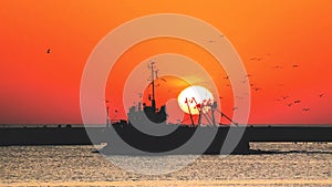 fishing ship with circling birds against the backdrop of the setting sun