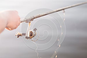Fishing at sunrise. Close-up fisherman hand with spinning fishing rod. Summer morning on river or lake. Copyspace