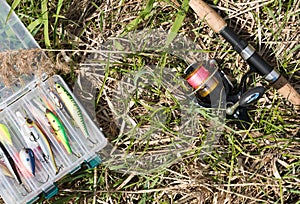 Fishing tackle box and spinning lie on the ground. Outdoor background