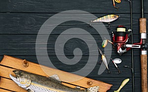 Fishing tackle - fishing spinning, hooks and lures on darken wooden background. Top view