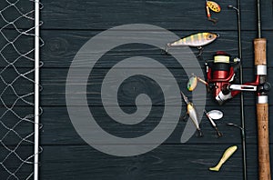 Fishing tackle - fishing spinning, hooks and lures on darken wooden background. Top view