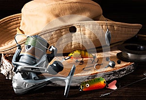 Fishing tackle. Hook, hat, fishing reel, lures on darken wooden background. Still life