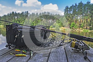 Fishing tackle set. Spinning rod with reel and lures on wooden platform on forest lake