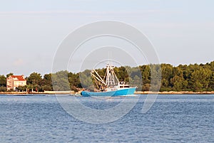 The fishing vessel for squid extraction returns in the early morning sailing past the green shore. Catch of cephalopods in the