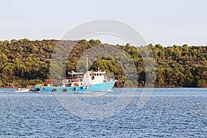 The fishing vessel for squid extraction returns in the early morning sailing past the green shore. Catch of cephalopods in the