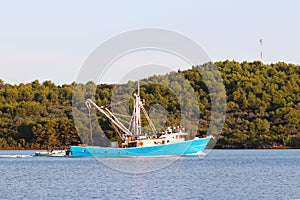 The fishing vessel for squid extraction returns in the early morning sailing past the green shore. Catch of cephalopods in the