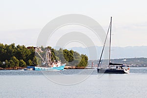 The fishing vessel for squid extraction returns in the early morning sailing past the green shore and sailing yacht. Catch of