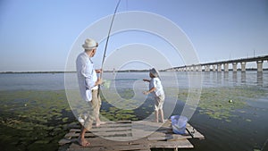 Fishing weekend of happy family, father and child in straw hats with spinning fun at river on pier while relaxing in