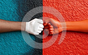 Fist bump gesture between red and white hands against colorful wall background symbolizing unity, diversity, and racial photo