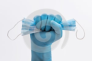 Fist Hand in medical blue latex protective glove holding a medical mask on white background