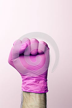 A fist in a medical glove. Doctor`s hand in a pink medical glove on a light background