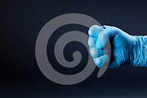 Fist of right man hand in a blue medical glove on a black background