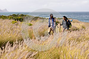 Fit afrcan american couple wearing backpacks nordic walking with poles in mountain countryside