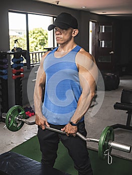A fit asian guy does upright rows with an EZ curl bar at an open air gym. Traps upper back and shoulder exercise. Starting
