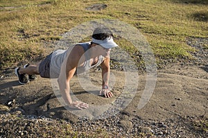 A fit asian guys does pushups on a barren rock surface after a trail run or hike in the countryside