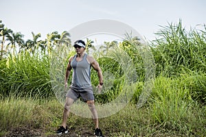 A fit asian male doing jump squats at a grassy field. Working out and training outdoors. Leg workout or calisthenics