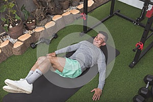 A fit asian man performs lying oblique twists on a black mat. Core workout at his home gym