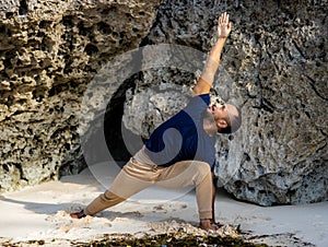 Fit Asian man practicing yoga on the beach. Standing pose Parivrtta Parsvakonasana. Revolved Side Angle Pose. Strong flexible body