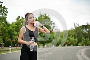 A fit Asian woman in sportswear wipes sweat from her face and neck with a towel