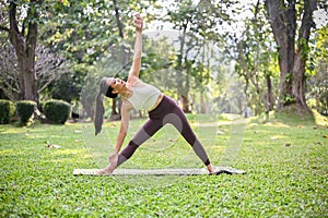 Fit Asian woman training in the garden, practicing Revolved triangle or Triangle forward  yoga pose