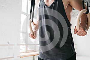 Fit athlete exercises on crosstraining rings in light hall