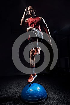 Fit athlete performing exercise on gymnastic hemisphere bosu ball on dark studio