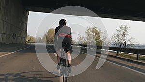 Fit athletic cyclist riding bicycle. Back follow shot. Young bike rider training on bicycle. Cycling concept