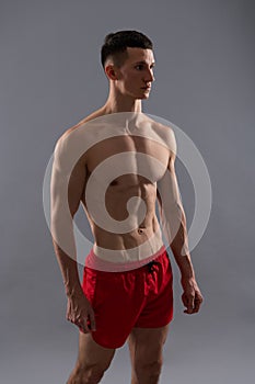 Fit athletic guy with muscular torso in sports shorts grey background, man