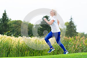 Fit athletic mature woman running alongside reeds