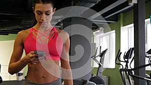 Fit athletic mixed race woman is walking texting sms in sport gym on phone