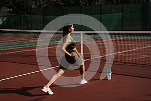 Fit attractive girl dressed in sportswear is training outside. Young woman doing lunges outdoors.