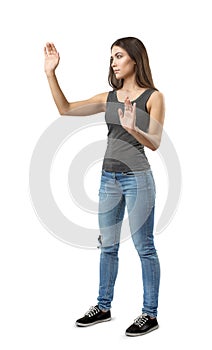 Fit beautiful woman in gray top and blue jeans standing in half-turn posing with hands raised as if touching invisible