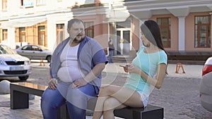 Fit beautiful woman ignoring fat man sitting on bench, sad unconfident bachelor