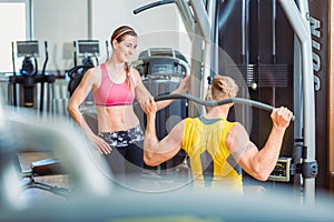 Fit beautiful woman smiling with admiration at a strong man in the gym