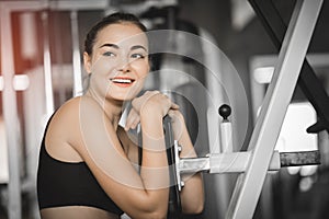Fit beautiful young woman exercise workout on machine in gym. Glad smiling girl is enjoy with her training process.