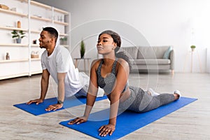 Fit black couple doing yoga cobra pose or pilates on mat indoors. Stay home hobbies