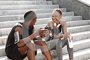 Fit Black Couple Taking Rest After Workout Outdoors, Sitting On Urban Stairs