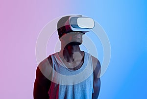 Fit black guy wearing VR headset, exercising with virtual reality gear in neon lighting