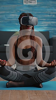 Fit black woman wearing virtual reality headset while sitting on yoga map