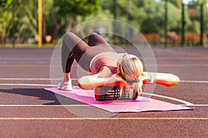 Fit blond woman training on mat outdoor summer day, using foam roller massager on her shoulders for relaxation