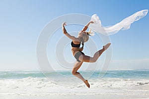 Fit blonde jumping gracefully with scarf on the beach