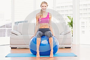 Fit blonde sitting on exercise ball smiling at camera